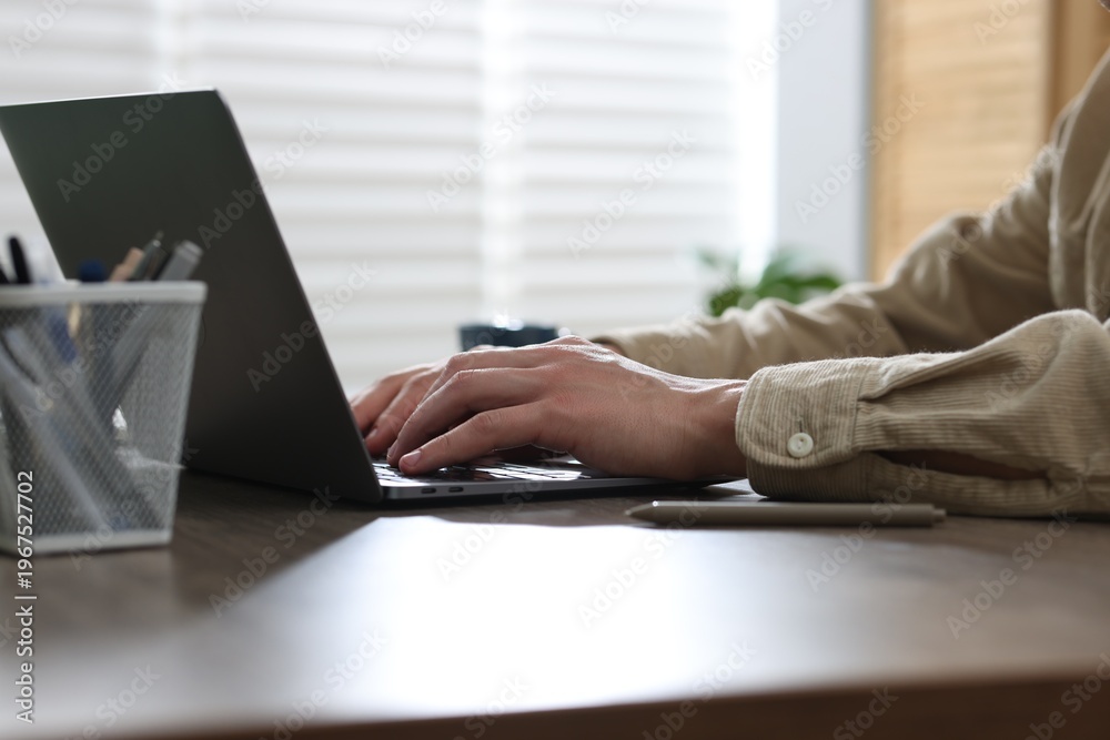 Fototapeta premium Man working on laptop at wooden desk in office, closeup