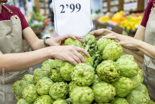 Shop assistants arranging fresh artichokes in grocery store