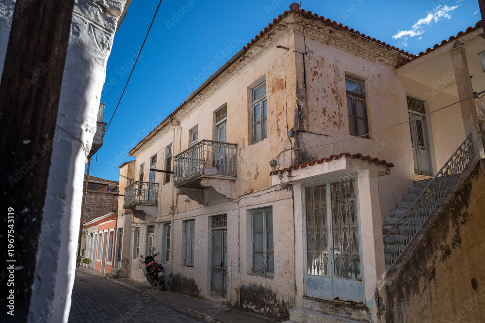 Obraz premium Street lined with traditional stone houses in Leonidio, Greece, captured on a sunny day. Authentic Mediterranean village architecture with warm light, historic character, and peaceful atmosphere.