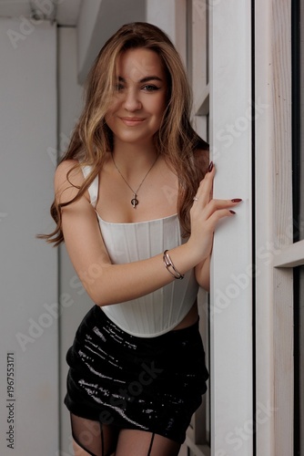 Woman posing by a window in a stylish outfit with a playful smile during a photo session at home