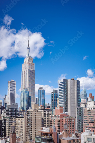 View of New York City skyline showcasing iconic Manhattan landmarks, buildings and skyscrapers on sunny day with clear blue sky.