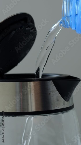 Domestic scene with water flowing into container. Morning kitchen routine involving filling glass vessel with water. Closeup of water flowing from bottle into glass kettle during morning prep