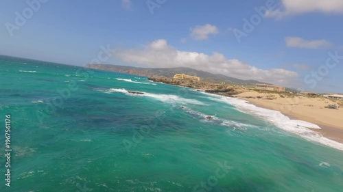 High drone view of beach near Lisbon, Portugal. Vehicle tracks drawn in the sand meet soft Atlantic waves. Aerial shot showing natural patterns and contrast between land and sea.