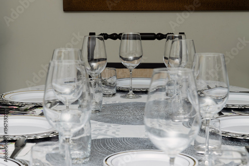 Elegant dining table set for eight with white tablecloth, silver charger plates, glassware and cutlery arranged for formal dinner at home