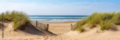 Sand dunes with green grass and a wooden fence creating a pathway to the tranquil ocean and a wide sandy beach