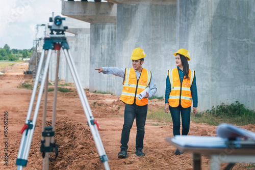 Team of two survey engineers in hard hats and safety vests are actively engaged in project planning on construction site.