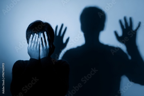 Person hides their face with hands while a large shadow appears on the wall.