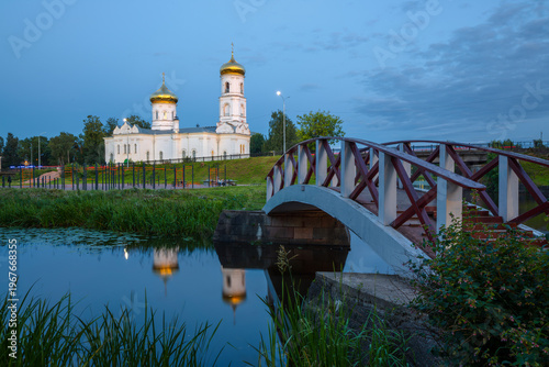 Vyshny Volochyok, Tver region, Russia. View of the wooden pedestrian bridge over the Obvodny Canal and the Epiphany Cathedral, located on an island surrounded by canals. Evening summer landscape.