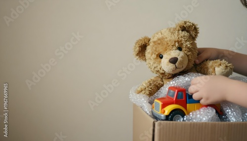 A child is packing a teddy bear into a box, with moving supplies like tape and bubble wrap visible in the background