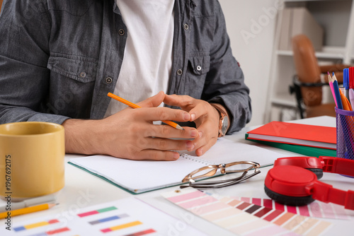 Fotografía Young businessman with color palettes, cup of coffee and notebook on table at of