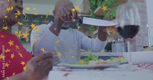 Carving man light sweater slicing roast with knife at home table, partner red top holding fork