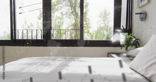 Showing white bed filling frame and casting shadows in bedroom with bedside table and potted plant