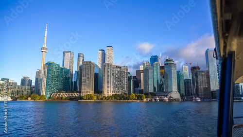 A vibrant view of the Toronto skyline from the water, featuring the CN Tower and modern waterfront skyscrapers under a clear blue sky
