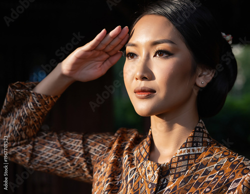 Close-up portrait of an elegant Indonesian woman in traditional attire, bathed in warm sunlight, showcasing cultural beauty and refined grace with a respectful salute