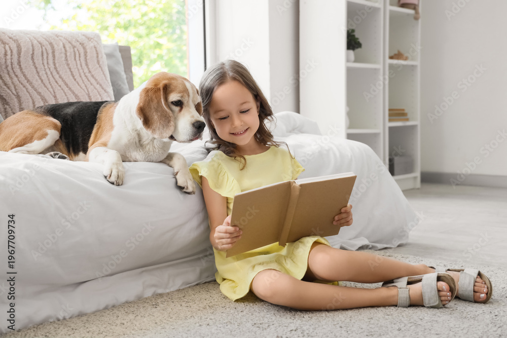 Obraz premium Cute little girl with Beagle dog reading book near bed in bedroom