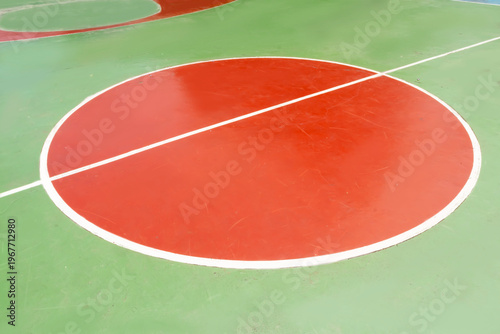 High angle view of a red center circle on a green outdoor basketball court with white lines.