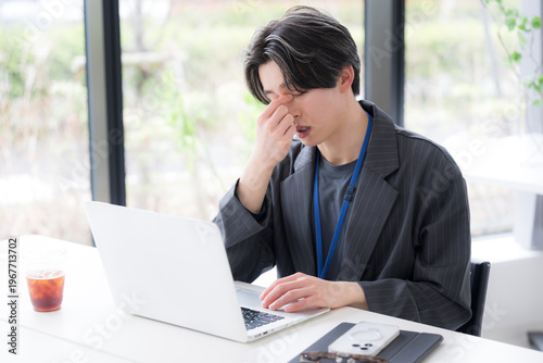 仕事の疲れで目を押さえる若手社員のストレスと体調不良のシーン　眼精疲労や目の疲れのビジネスイメージ