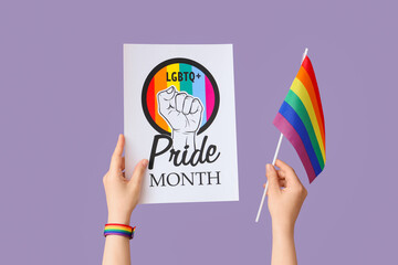 Female hands holding paper with text LGBTQ+ PRIDE MONTH and flag on lilac background