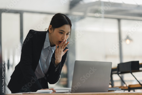 Obraz na płótnie Shocked Asian businesswoman looking at laptop screen with open mouth in a modern corporate office