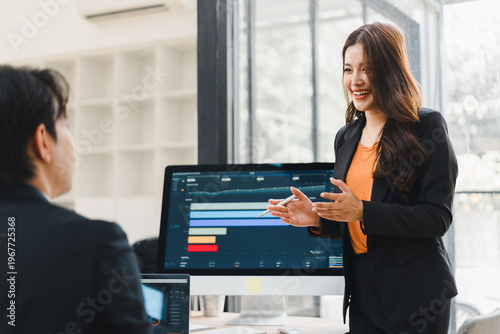 Fotografija Smiling Asian businesswoman presenting data charts on a computer monitor to a ma