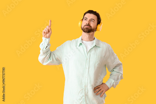 Handsome man in headphones pointing at something on yellow background