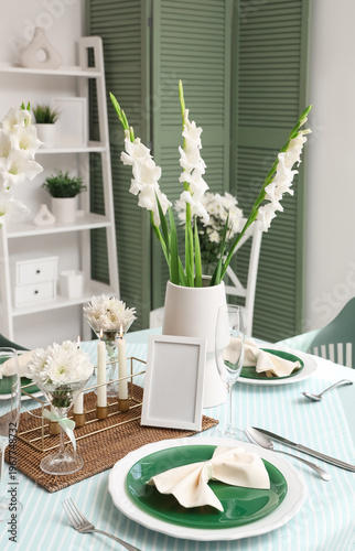 Table setting with white Gladiolus flowers and burning candles in room