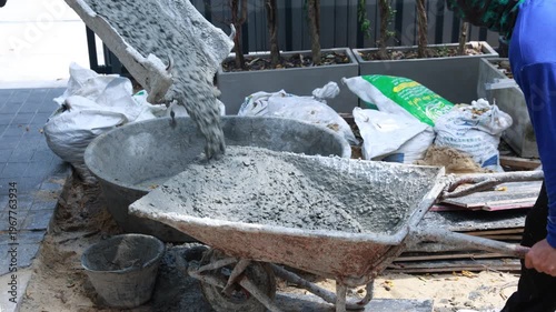 Pouring wet cement concrete from a truck mixer chute into a large mixing tub at a residential construction site. Professional building process and infrastructure development.