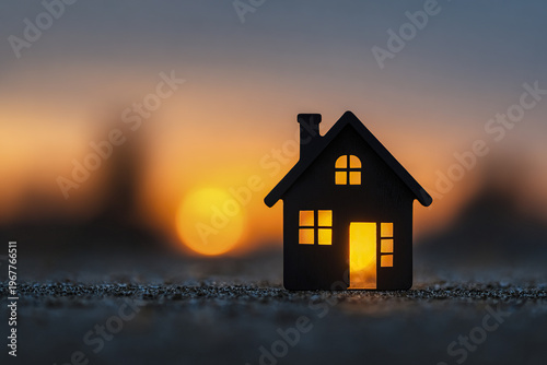 Miniature house silhouette with glowing sunrise behind, symbolizing mortgage approval and new home beginning in warm early morning light