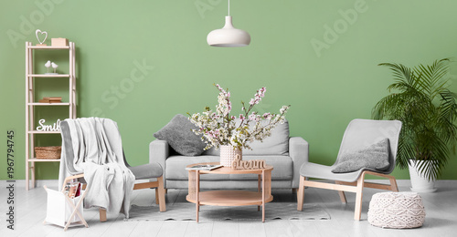 Sofa with armchairs, coffee table and vase of blooming branches near green wall in living room