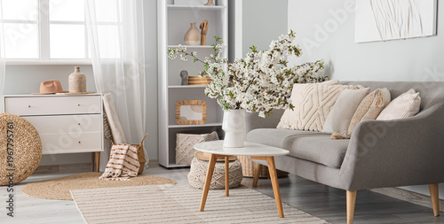 Interior of light living room with sofa and flowering branches