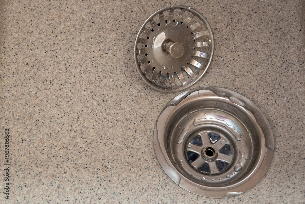 Obraz premium Stainless steel sink drain with strainer and drain cover on a textured countertop surface in a modern kitchen setting