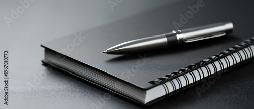 Black Notebook with Silver Pen on Dark Desk Surface