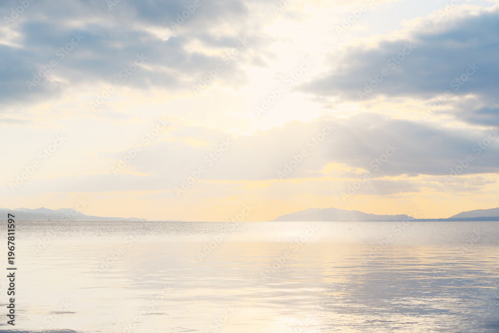 Fototapeta premium 夕焼けの湖と山並み、静穏な水面に映る光の帯