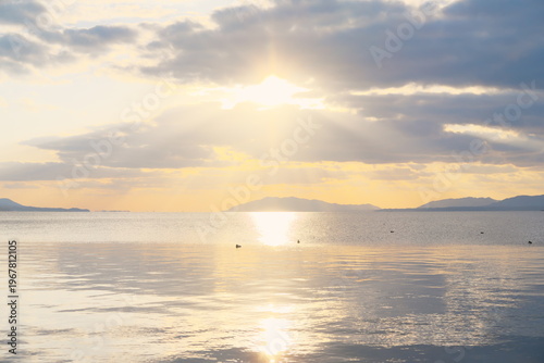 夕焼けの湖に射し込む光と山並み - 静寂な水面に映る空