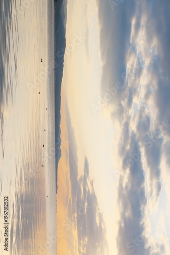 夕暮れ時の静かな湖面と遠くの山並み、空に浮かぶ雲