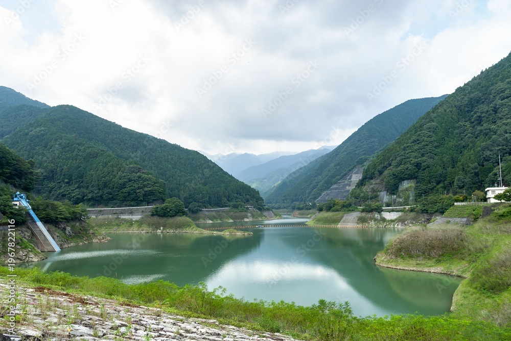 Fototapeta premium 埼玉県飯能市にある名栗湖（有間ダム）の山々に囲まれた穏やかな水面/Calm Water Surface of Lake Naguri Surrounded by Mountains