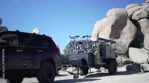 Setting up a teardrop camper trailer near large rocks in Joshua Tree National Park with bicycles on top for a day in the desert