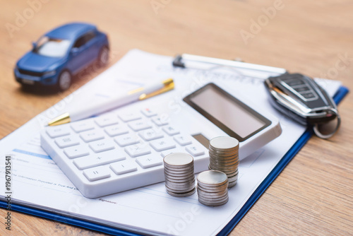 Car insurance document on clipboard with white calculator, stacked coins, blue toy car and modern car key on wooden desk. Concept auto insurance premium calculation and vehicle finance planning.