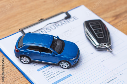Close up of automobile insurance application form with miniature car model and electronic keychain. Concept vehicle protection, motor legal services, loan agreement and financial security.