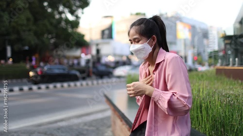 Person wearing mask in toxic urban air, monitoring pollution levels on device, highlighting health risks, environmental hazards, smog, and city pollution concerns.
