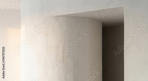 A minimalist interior shot shows a curved wall and an opening leading into a darker space, bathed in soft, warm light.