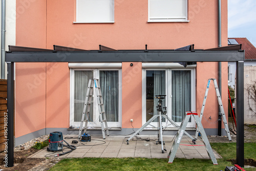 Fotografie Workers install patio roofing with steel and glass
