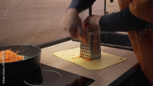 The hands of a male householder grate carrots.