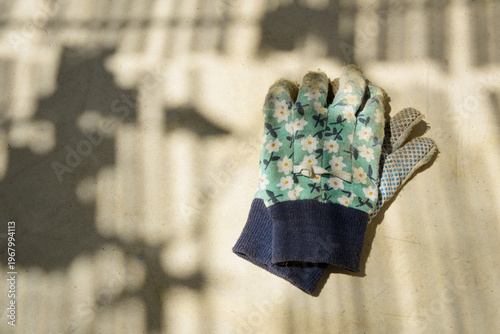 Vieux gants de jardin à motifs floraux en coton, posés sur une table, sous l'ombre des canisses