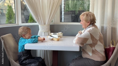 Wallpaper Mural An elderly woman and a young boy sit at a cafe table, smiling warmly at each other. They share a happy, connected moment in a bright, cozy room. Their joy makes the atmosphere feel very sweet. Torontodigital.ca