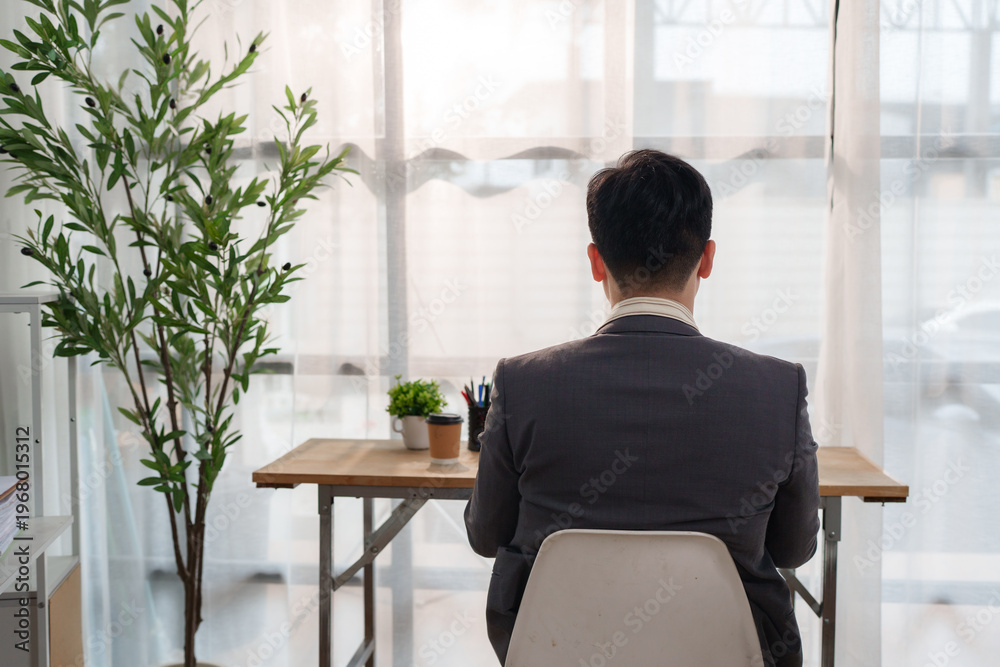 Obraz premium Businessman sitting at desk looking out window contemplating