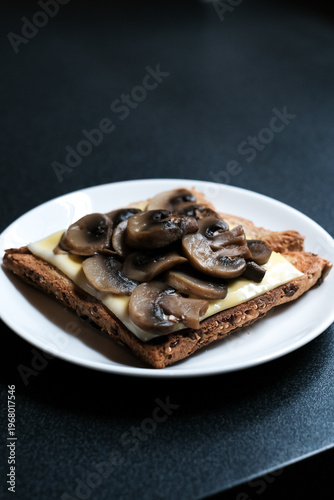 homemade toasted sandwich with cheese and brown mushrooms on black table.