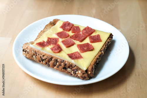 Toasted sandwich sausage and cheese in a white plate on wooden table.