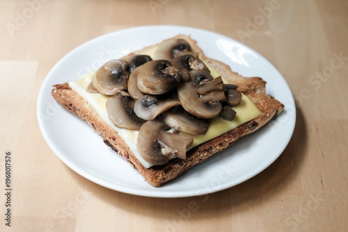 Toasted sandwich with cheese and brown mushrooms in a white plate on wooden table.