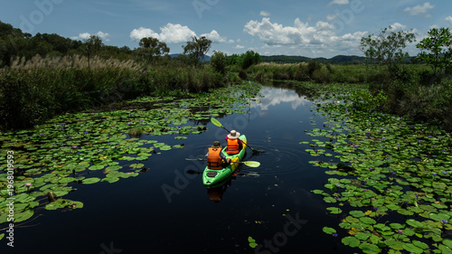 Fotografie Two People Paddle Green Tandem Kayak Along Narrow Waterway Through Dense Field O